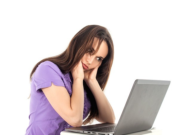 An anxious woman wearing a purple shirt in front of a computer