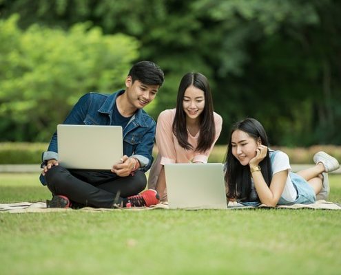 One man and two women having fun with their laptops in a park