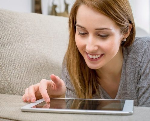A woman browsing on her tablet device on a sofa